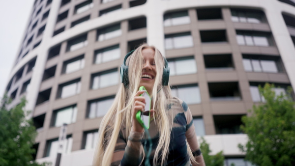 Video of a Generation Z girl student listening to music via headphones outdoors in the city. Student spending free time online and alone. Concept of gen Z as loneliest generation.