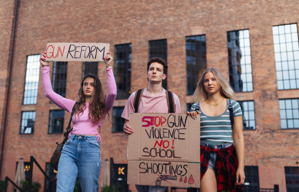 Generation Z activists with banners protesting on the street. Young zoomers students marching through the city demonstrate against climate change. Protesters demanding gun control, racial and gender equity. Concept of power of friendship and social strength of gen Z.