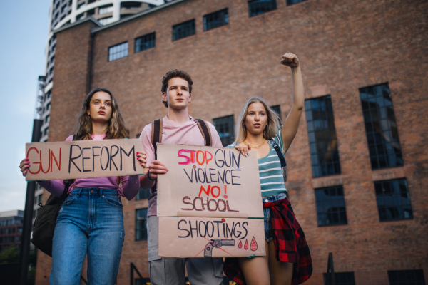 Generation Z activists with banners protesting on the street. Young zoomers students marching through the city demonstrate against climate change. Protesters demanding gun control, racial and gender equity. Concept of power of friendship and social strength of gen Z.