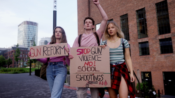 Generation Z activists with banners protesting on the street. Young zoomers students marching through the city demonstrate against climate change. Protesters demanding gun control, racial and gender equity. Concept of power of friendship and social strength of gen Z.