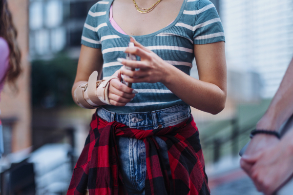 Close up of a young woman's injured wrist with a plastic brace on. Gen z girl in trendy outfit.