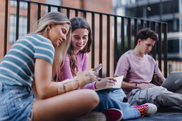 Group of generation Z students studying together outdoors after school. Young stylish zoomers working together on school project, preparing a presentation. Concept of power of friendship and importance of education of gen Z.