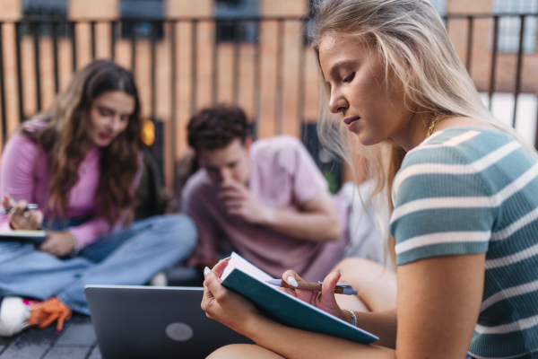 Group of generation Z students studying together outdoors after school. Young stylish zoomers working together on school project, preparing a presentation. Concept of power of friendship and importance of education of gen Z.