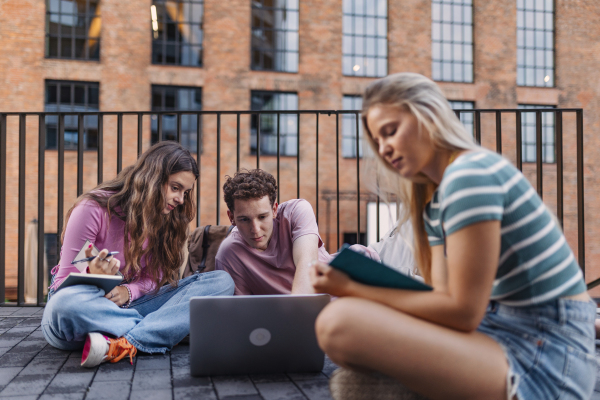 Group of generation Z students studying together outdoors after school. Young stylish zoomers working together on school project, preparing a presentation. Concept of power of friendship and importance of education of gen Z.