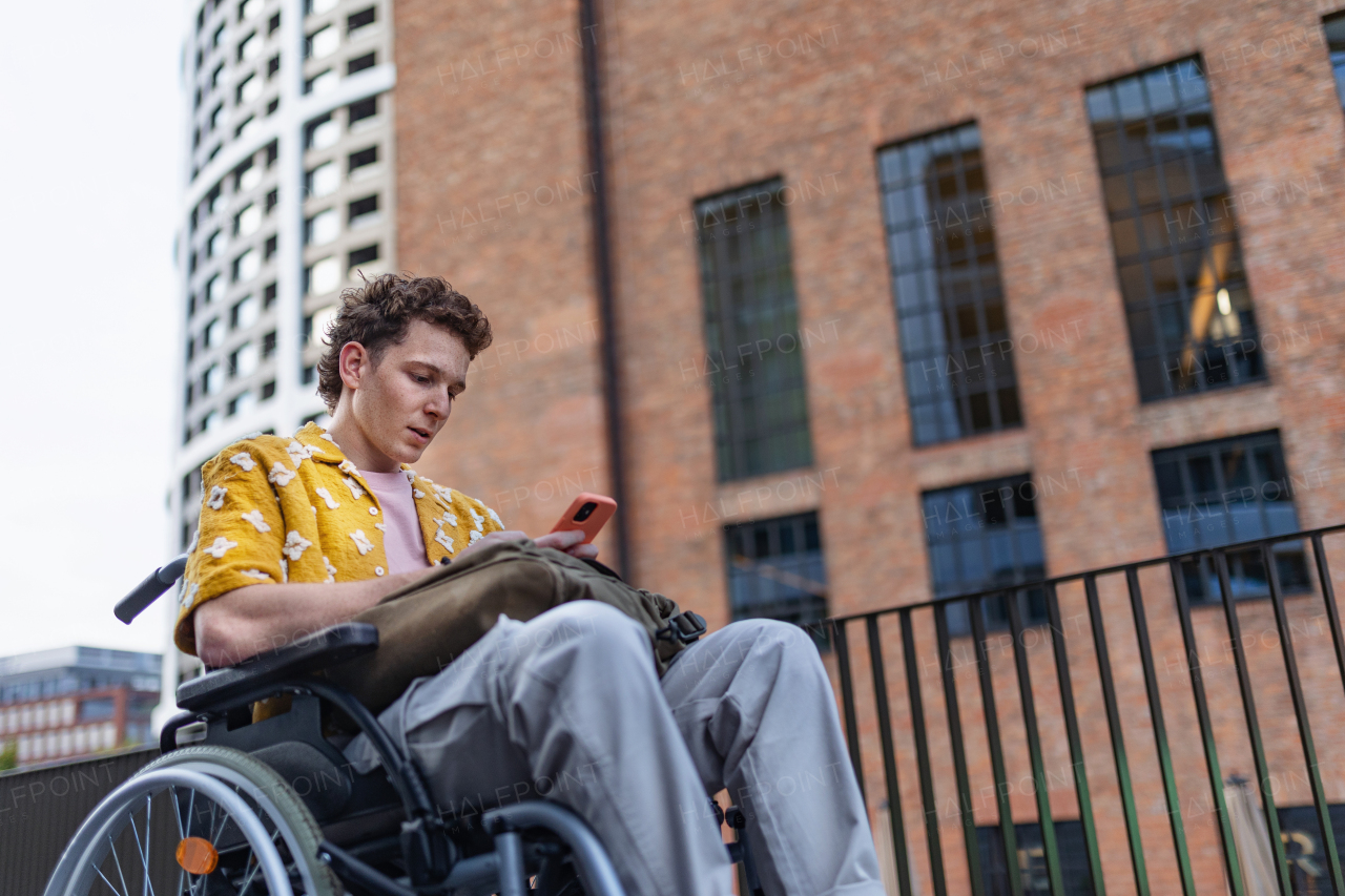 Gen Z boy in a wheelchair in the city using smartphone. Inclusion, equality, and diversity among Generation Z.