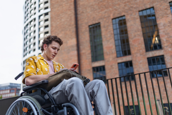 Gen Z boy in a wheelchair in the city using smartphone. Inclusion, equality, and diversity among Generation Z.