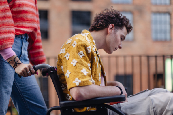 Sad gen Z boy in a wheelchair with friends in the city. Inclusion, equality, and diversity among Generation Z. Sadness and helplessness in the face of chronic illness.