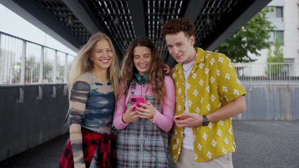 Generation z students hanging out together outdoors in the city. Young stylish zoomers are online, using smartphones, social media, taking selfies. Concept of power of friendship and social strength of gen Z. Low angle shot with copy space.