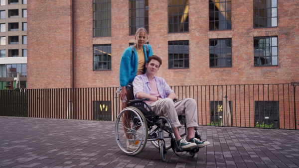 Handsome gen Z boy in a wheelchair with friend in the city. Inclusion, equality, and diversity among Generation Z.