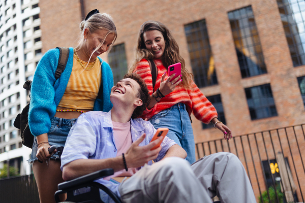 Handsome gen Z boy in a wheelchair with friends in the city. Inclusion, equality, and diversity among Generation Z.