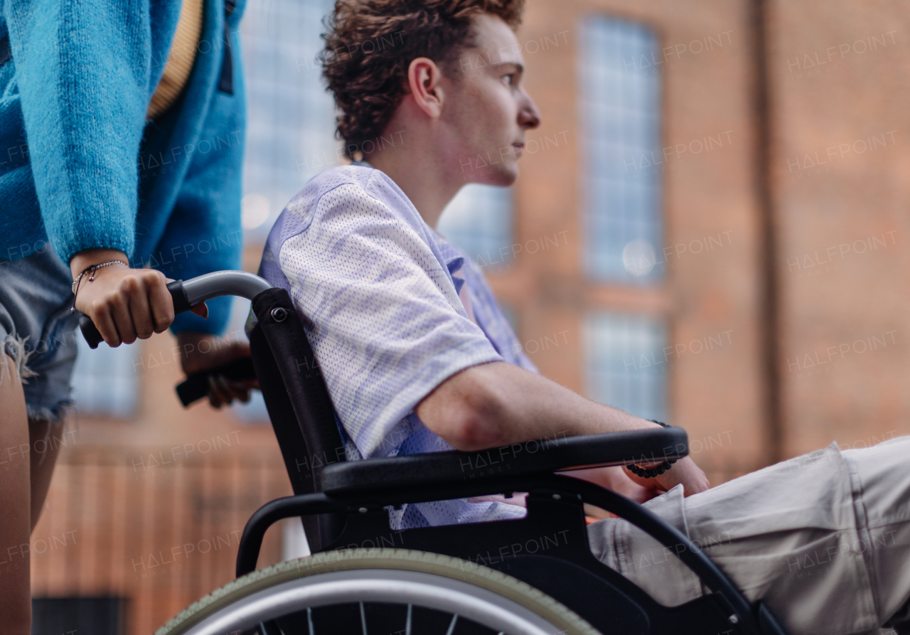 Sad gen Z boy in a wheelchair with friends in the city. Inclusion, equality, and diversity among Generation Z. Sadness and helplessness in the face of chronic illness.