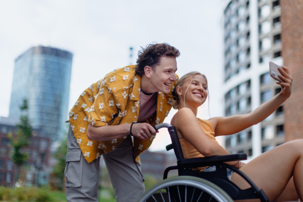 Beautiful gen Z girl in a wheelchair with her boyfriend taking selfie. Inclusion, equality, and diversity among Generation Z.