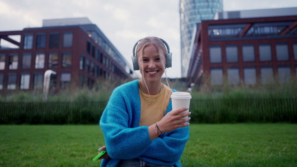 Video of a Generation Z girl student listening to music via wireless headphones outdoors in the city. Student spending free time alone, enjoying coffee in a reusable travel mug. Concept of gen Z as loneliest generation.