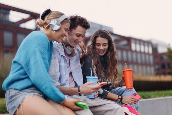 Generation z students hanging out together outdoors in the city. Young stylish zoomers are online, using smartphones, social media, taking selfies. Concept of power of friendship and social strength of gen Z.