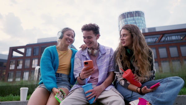 Generation z students hanging out together outdoors in the city. Young stylish zoomers are online, using smartphones, social media, taking selfies. Concept of power of friendship and social strength of gen Z.