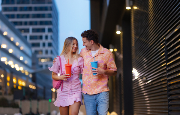 Gen Z couple in pink outfits leaving the cinema with drinks in hand. The young zoomers watched a movie addressing the topic of women, her position in the world, and body image.