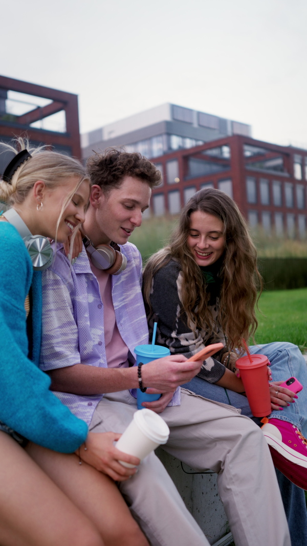 Generation z students hanging out together outdoors in the city. Young stylish zoomers are online, using smartphones, social media, taking selfies. Concept of power of friendship and social strength of gen Z.