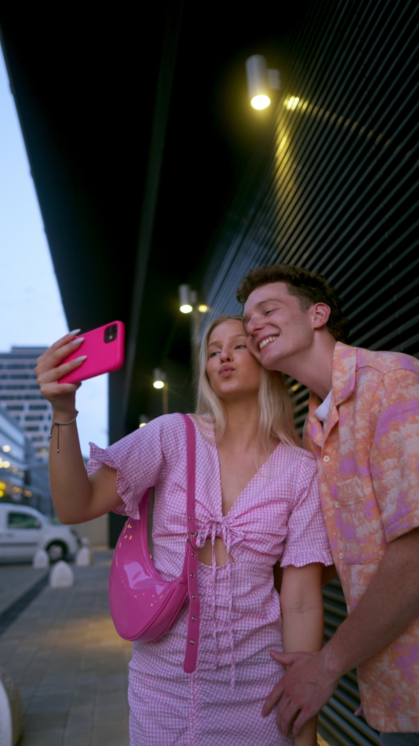 Gen Z couple in pink outfit taking selfie before going the cinema to watch movie. The young zoomer girl and boy watched a movie addressing the topic of women, her position in the world, and body image.