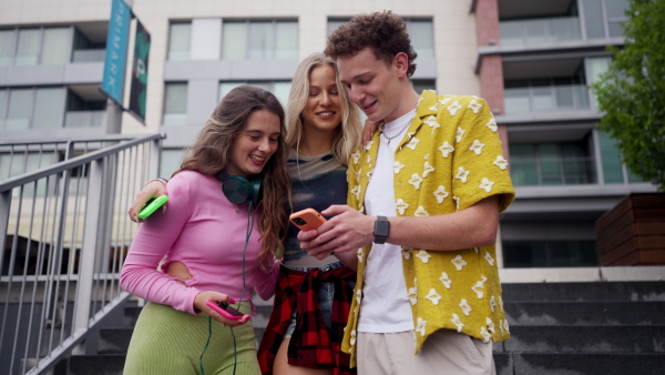 Generation z students hanging out together outdoors in the city. Young stylish zoomers are online, using smartphones, social media, taking selfies. Concept of power of friendship and social strength of gen Z. Low angle shot with copy space.