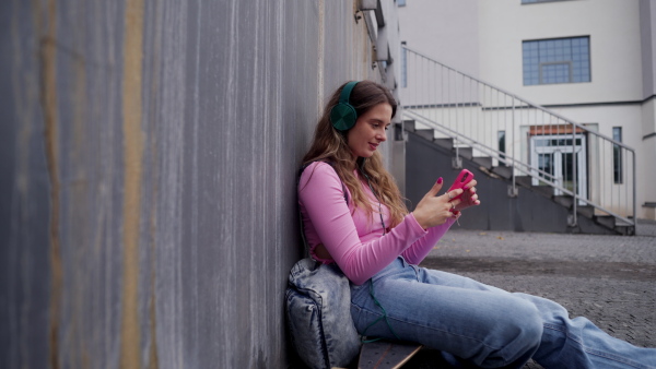 Video of generation z girl student sitting outdoors in the city. Student spending free time online and alone. Concept of gen Z as loneliest generation.