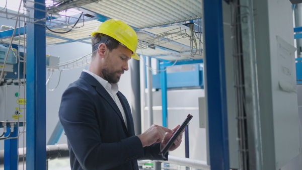 Inpector in factory with protective helmet checking processes on control panel.