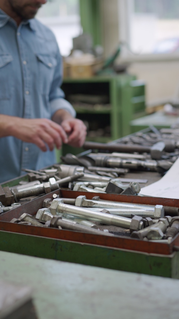 Industry worker man sorting metal drills in a warehouse, vertical footage.