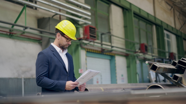 Engineer businessman with protective helmet in a factory, checking blueprints.