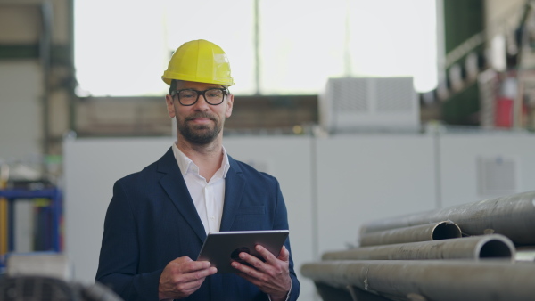 Engineer businessman with protective helmet in a factory, holding digital tablet and looking at camera.