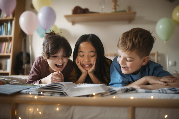 Three happy friends reading a book together in room.