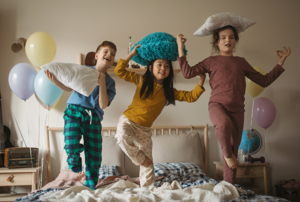 Three happy friends having fun with pillows on bed.