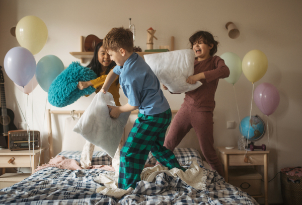 Three happy friends having fun with pillows on bed.