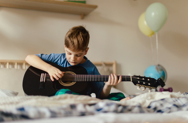 Happy boy playing on the guitar in the room.