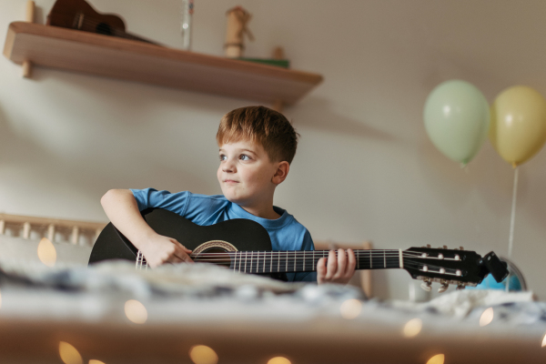 Happy boy learning to play guitar in the room by himself.