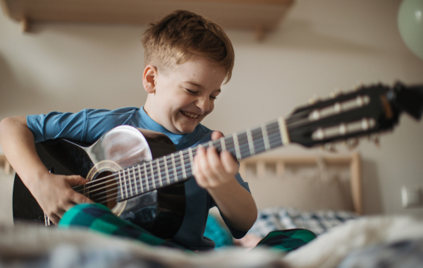 Happy boy playing on the guitar in the room.