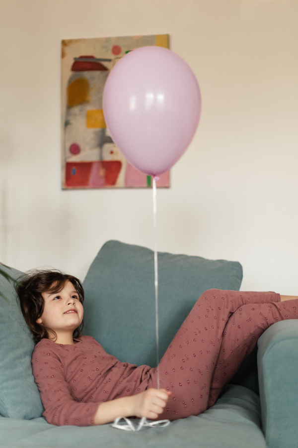 Little girl sitting on sofa with pink balloon.