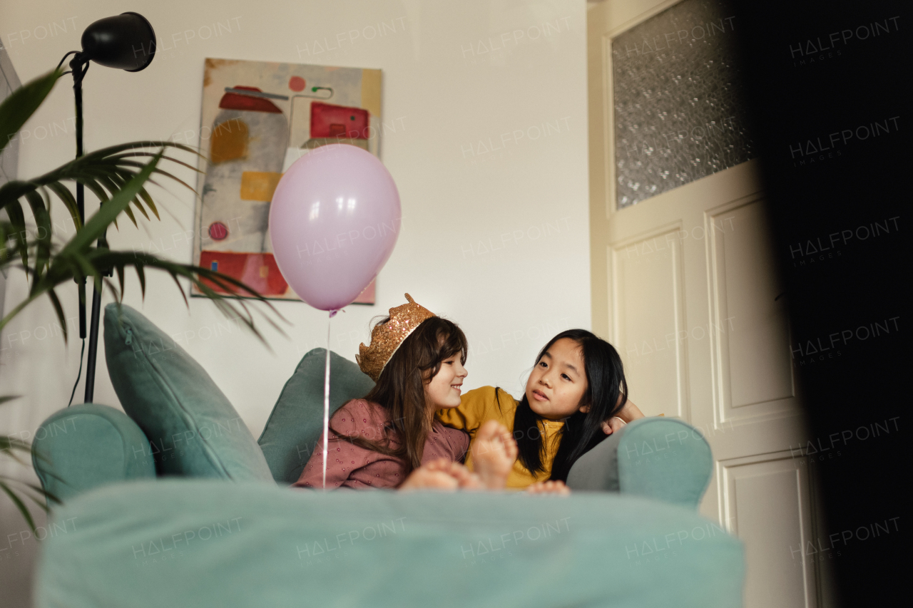 Little girls sitting and talking on sofa with pink balloon.