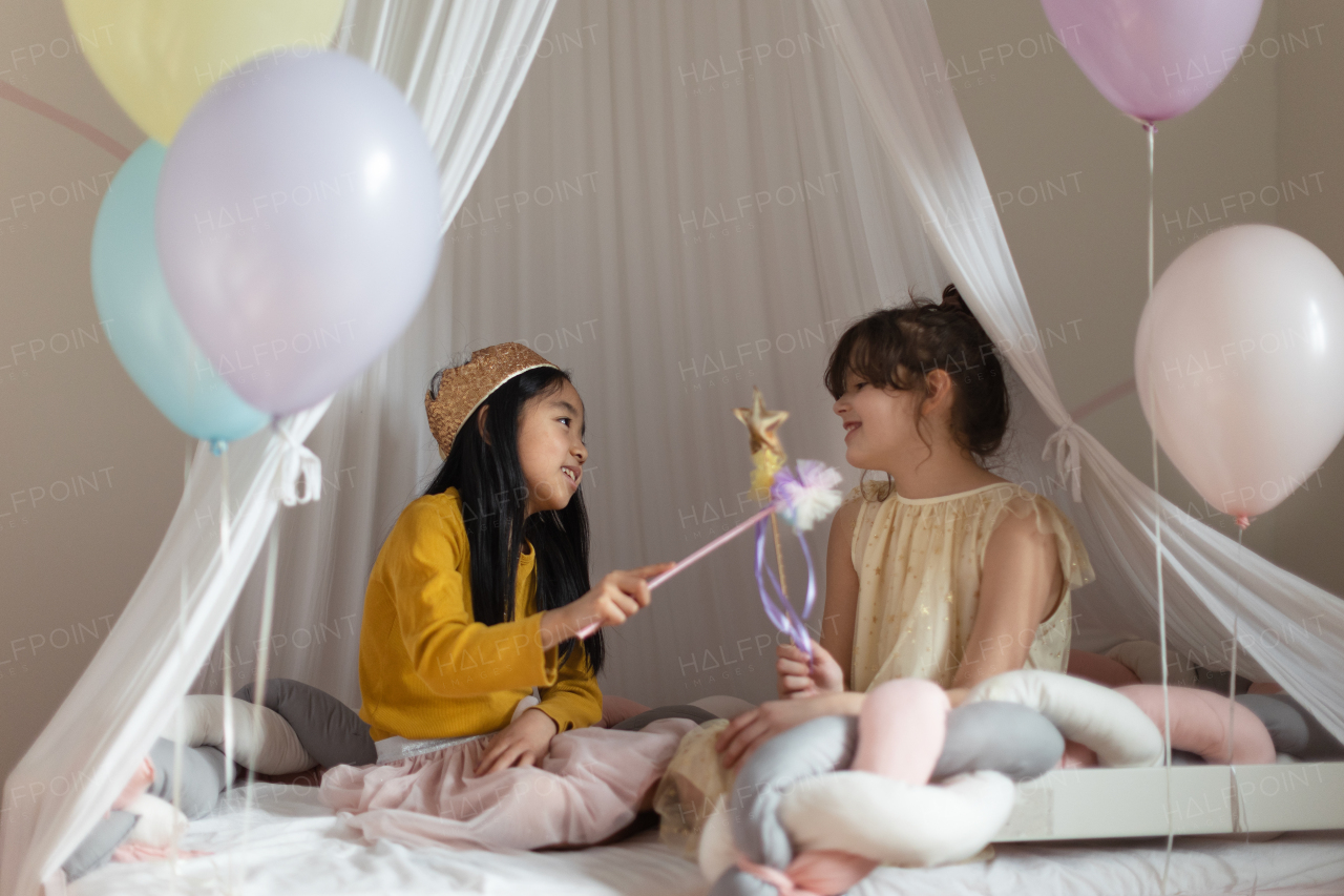 Happy girls playing princess with princess wands in indoor play tent.