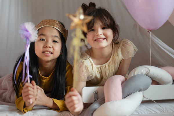 Happy girls playing princess with princess wands in indoor play tent.