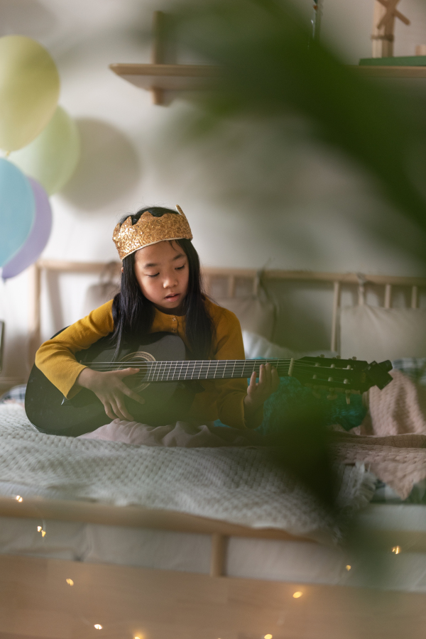 Little princess girl playing on the guitar in the room. Independent young girl learning to play the guitar by herself.