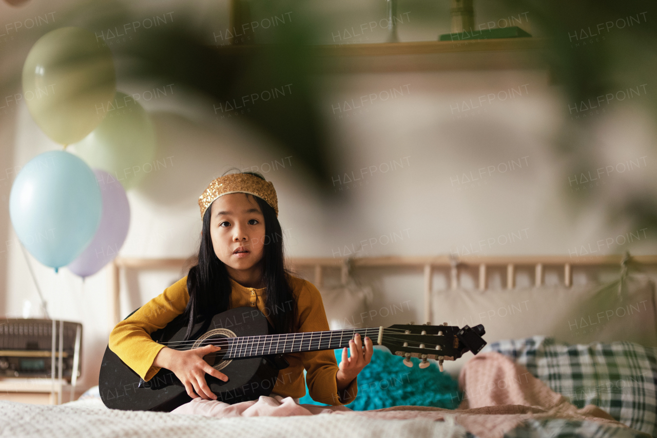 Happy girl playing on guitar in the room.