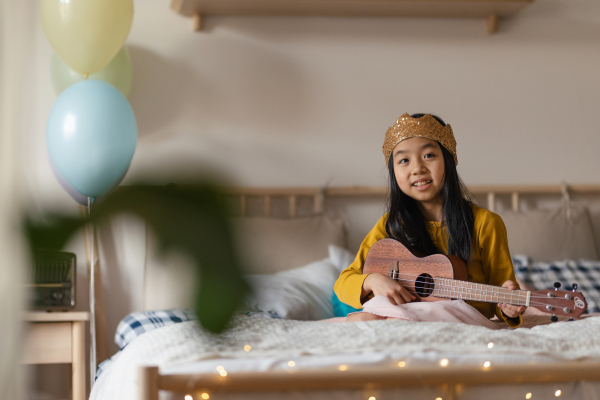 Happy girl playing on the ukulele in the room.