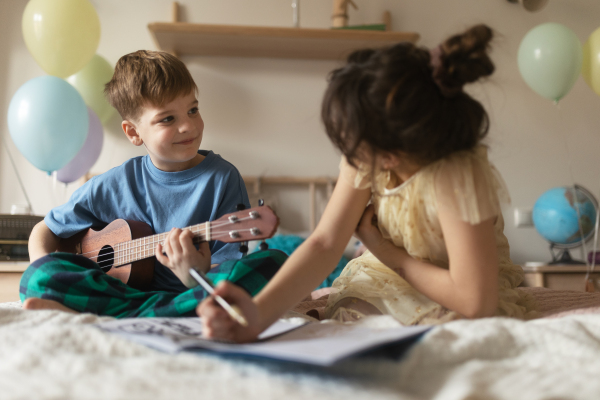 Sister and brother spend quality time together. Happy friends playing on the musical instuments and do the homework together.