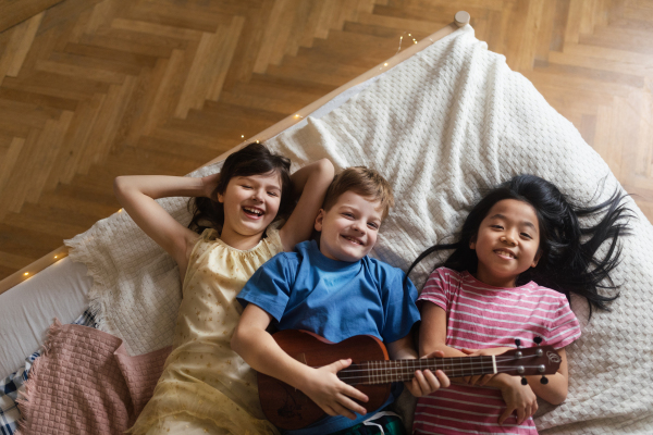 Top view of three happy friends lying in bed with ukulele.