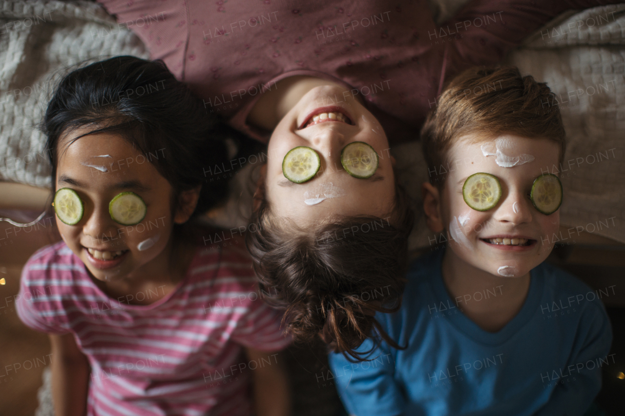 Top view of three happy friends lying in bed with beauty mask on face.