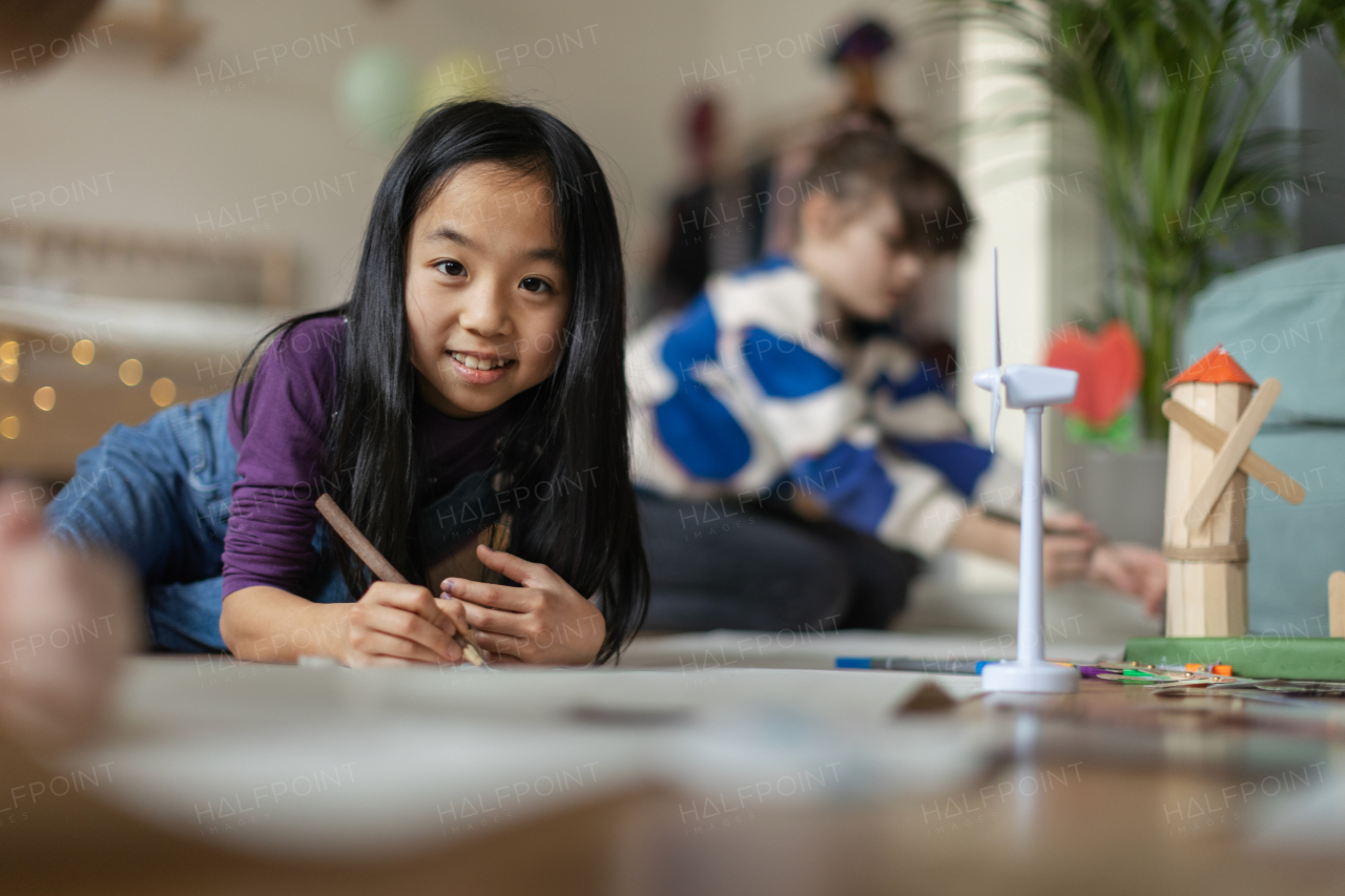 Portrait of a cute Asian girl working on her school project. Young girl lying on a floor and drawing.