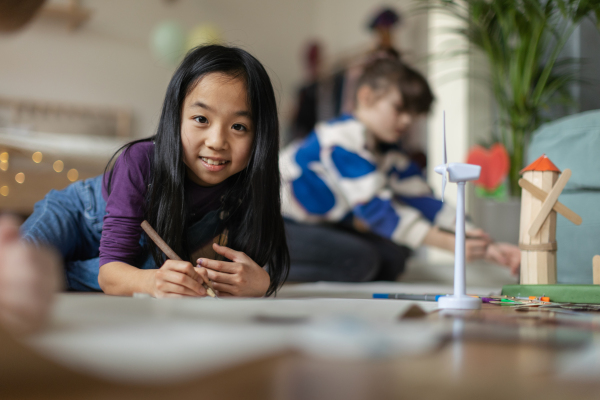 Portrait of a cute Asian girl working on her school project. Young girl lying on a floor and drawing.