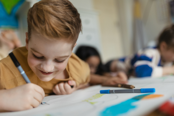 Portrait of young boy working on school project about wind energy with his classmates. Cute boy drawing with markers.