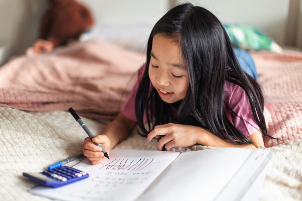 Little girl lying on a bed and doing the homework.