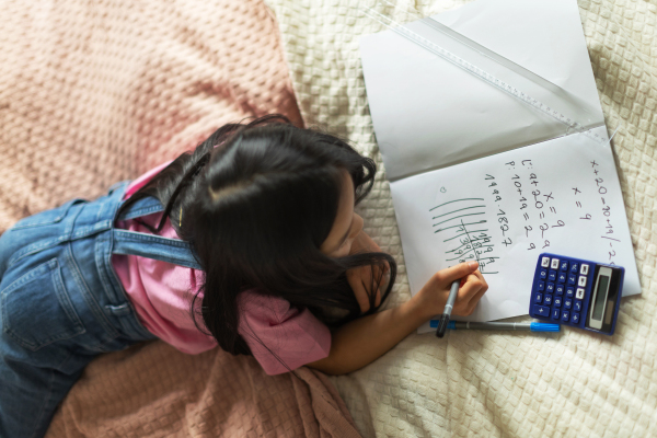 Top view of little girl lying on bed and learning math.