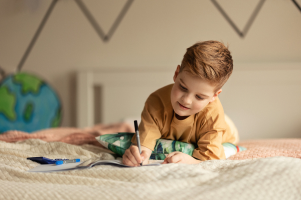 Little boy lying on a bed and doing the homework.